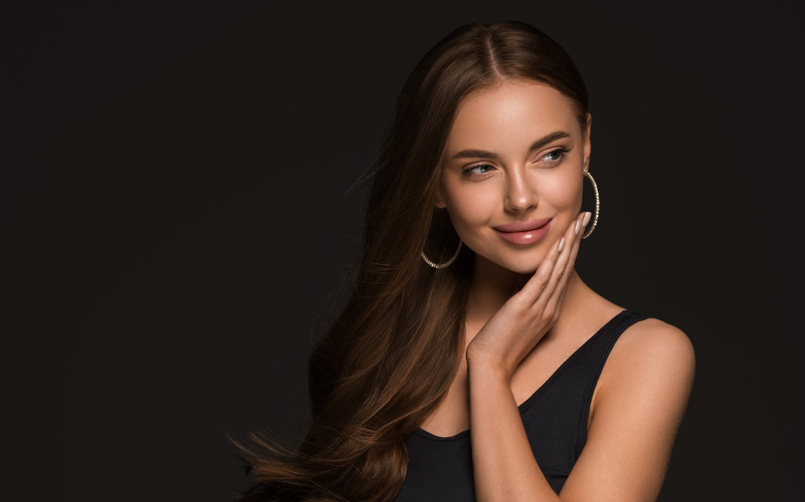 Beautiful woman with long healthy curly brunette hair earrings black dress black background